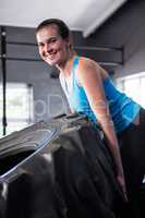 Portrait of smiling female athlete pushing tire in gym