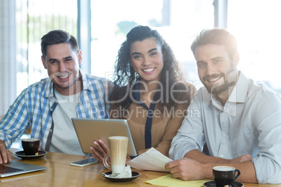 Smiling friends using digital tablet and laptop in cafÃ?Â©