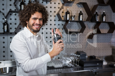 Happy waiter shaking drink in cocktail shaker in a bar