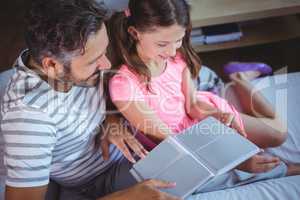 Father and daughter looking photo album on bed