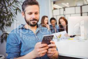 Businessman using mobile phone against female coworkers