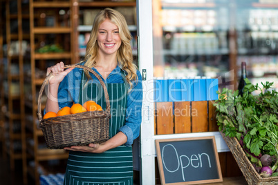 Smiling female staff holding basket of fruit in supermarket