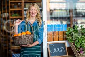Smiling female staff holding basket of fruit in supermarket