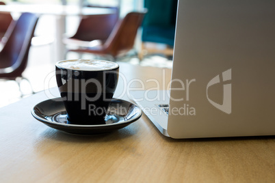 Close -up of cup of coffee and laptop on table