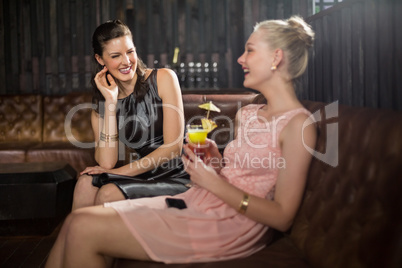 Female friends interacting with each other while having cocktail