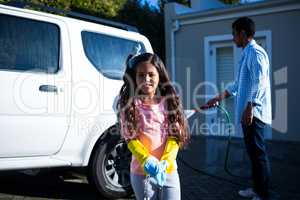 Daughter holding sponge while father doing carwash