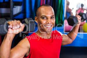Portrait of happy man lifting dumbbell in gym