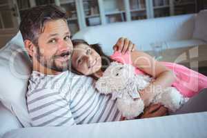 Smiling father and daughter sitting on sofa with a teddy bear