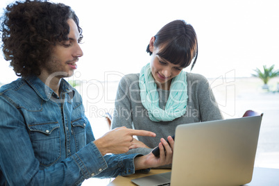 Couple using mobile phone with laptop on table