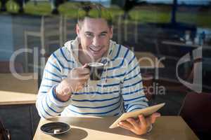 Portrait of smiling man using digital tablet while having coffee