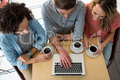 Three friends with coffee cups using a laptop