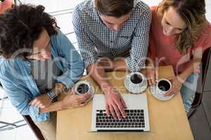 Three friends with coffee cups using a laptop