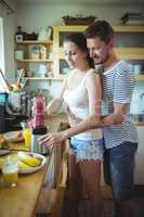 Man embracing woman from behind while preparing watermelon smoothie in the kitchen