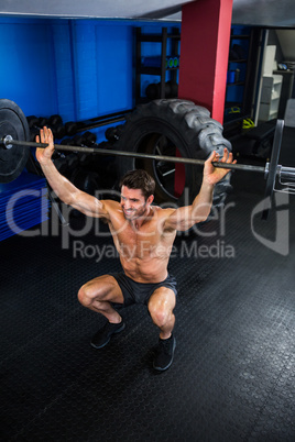 shirtless man lifting barbell in gym