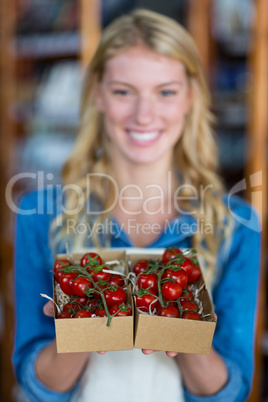 Smiling female staff holding box of cherry tomato in super market