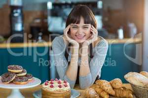 Portrait of waitress sitting at counter with sweet food on table