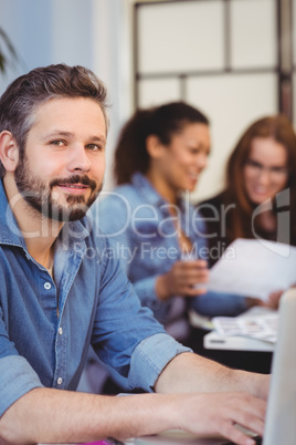 Confident businessman using laptop against female coworkers