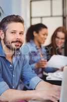 Confident businessman using laptop against female coworkers