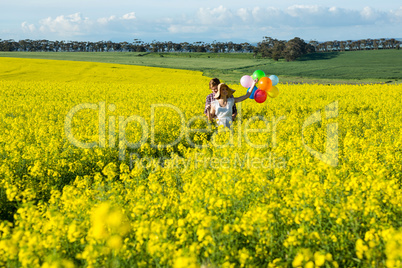 Couple holding colorful balloons in mustard field