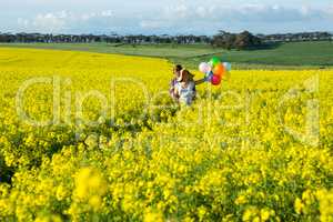 Couple holding colorful balloons in mustard field