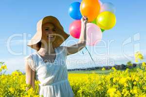 Woman holding colorful balloons in mustard field