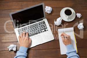 Man using laptop while writing on notepad