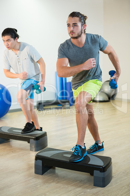 Two men doing step aerobic exercise with dumbbell on stepper