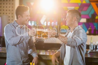 Two male friends toasting beer mugs at bar counter