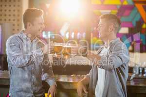 Two male friends toasting beer mugs at bar counter