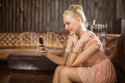 Beautiful woman sitting on sofa and using mobile phone