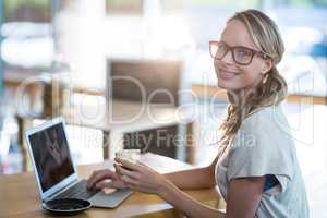 Smiling woman using a laptop while having cup of coffee in cafe