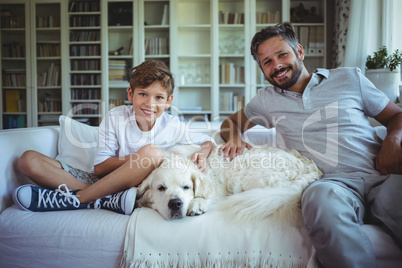 Father and son sitting on sofa with pet dog in living room
