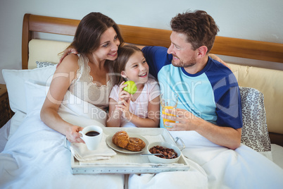 Parents sitting on bed with daughter and having breakfast