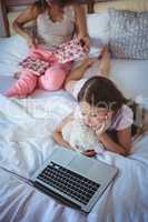 Daughter using laptop on bed and mother opening her present
