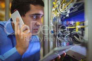 Technician talking on mobile phone while analyzing server