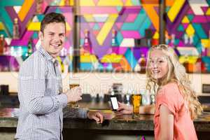 Smiling couple standing with beer glass at bar counter