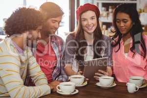 Group of friends using digital tablet while having cup of coffee