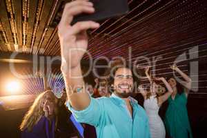 Man taking a selfie from mobile phone while friends dancing on dance floor