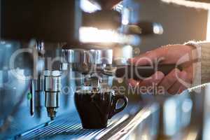 Waiter making cup of coffee at counter in kitchen