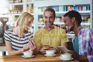 Three friends using mobile phones while having cup of coffee