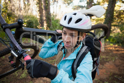 Female mountain biker carrying her bicycle in the forest