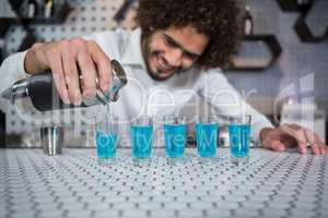 Bartender pouring cocktail into shot glasses