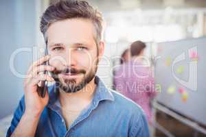 Portrait of confident businessman listening to cellphone at creative office