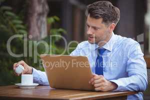 Handsome businessman having tea while using laptop