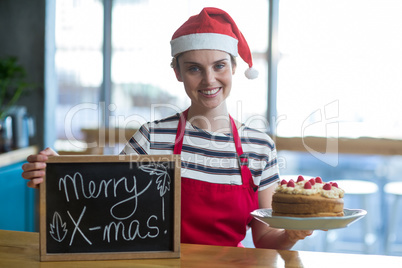 Portrait of waitress holding slate with merry x-mas sign and cake in cafÃ?Â©
