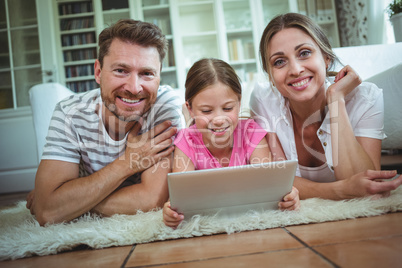 Parents and daughter lying on rug and using digital tablet