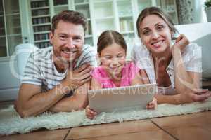 Parents and daughter lying on rug and using digital tablet