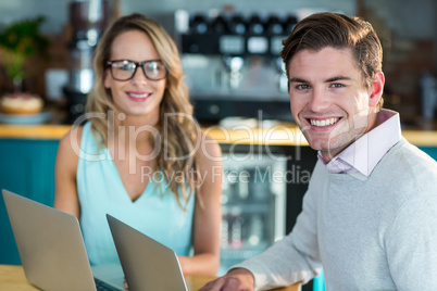 Smiling man and woman using laptop in cafe