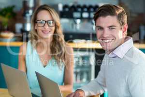 Smiling man and woman using laptop in cafe