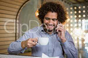 Man talking on mobile phone while having cup of tea